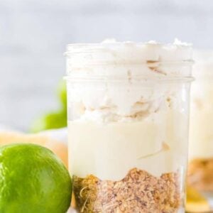 A mason jar filled with key lime mousse featuring a crumbly graham cracker crust, creamy filling, and whipped topping, with a fresh lime placed beside the jar.