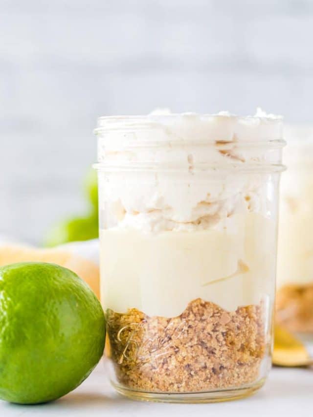 A mason jar filled with key lime mousse featuring a crumbly graham cracker crust, creamy filling, and whipped topping, with a fresh lime placed beside the jar.