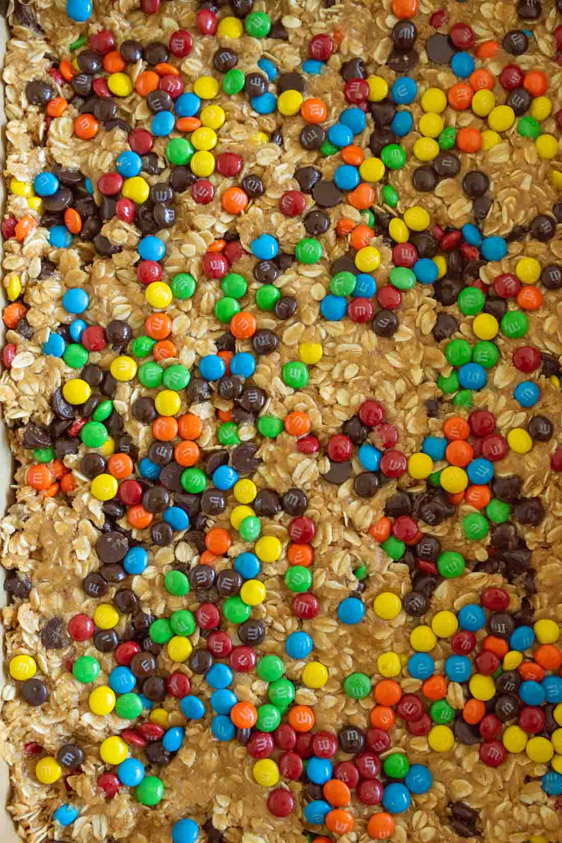 Cookie bars topped with colorful M&M candies, oats, and chocolate chips, creating a textured and vibrant dessert surface.