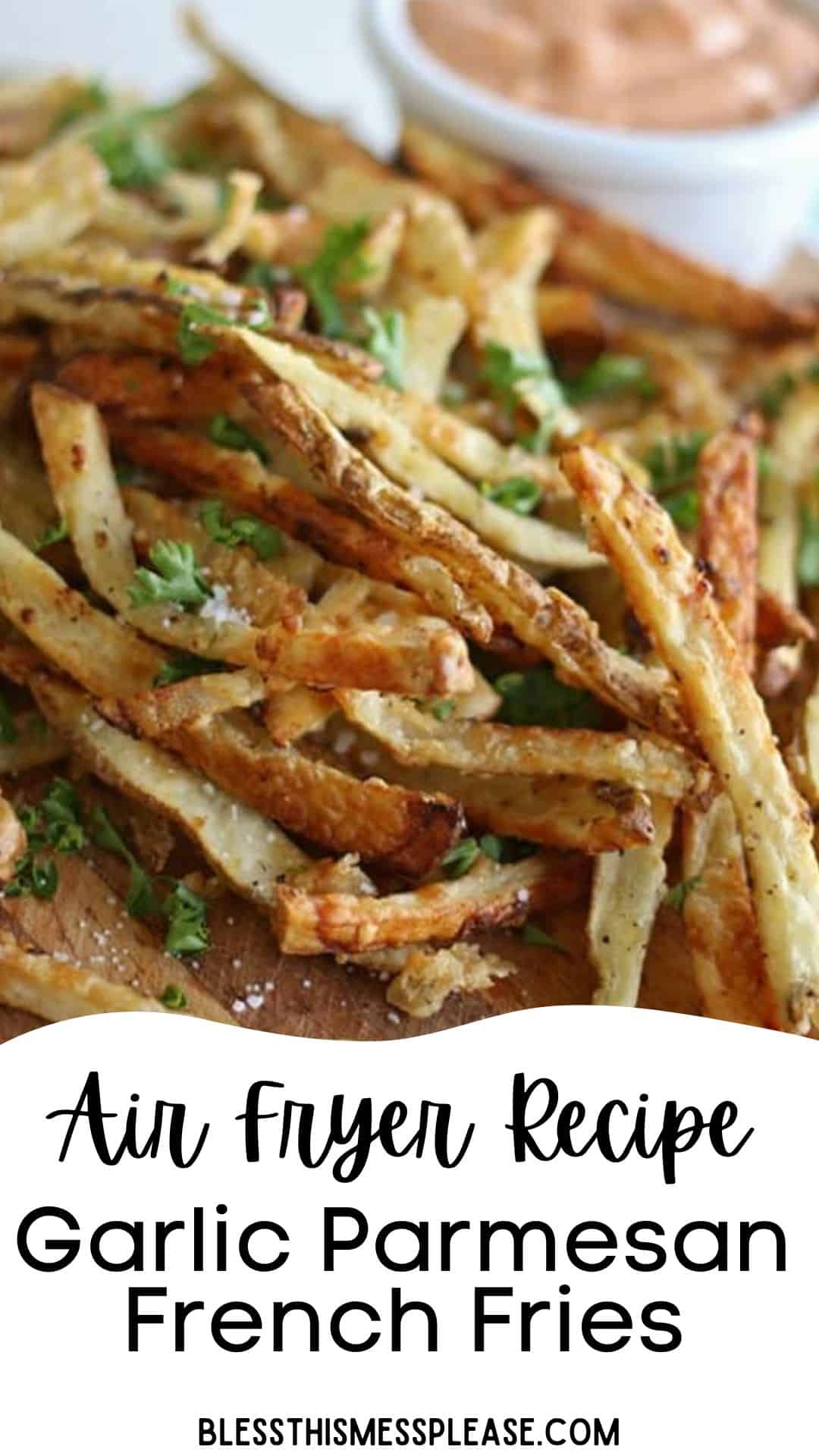 A close-up of crispy garlic parmesan french fries made in the air fryer, garnished with parsley, with a bowl of dipping sauce in the background. Text on the image reads: Air Fryer Recipe Garlic Parmesan French Fries.