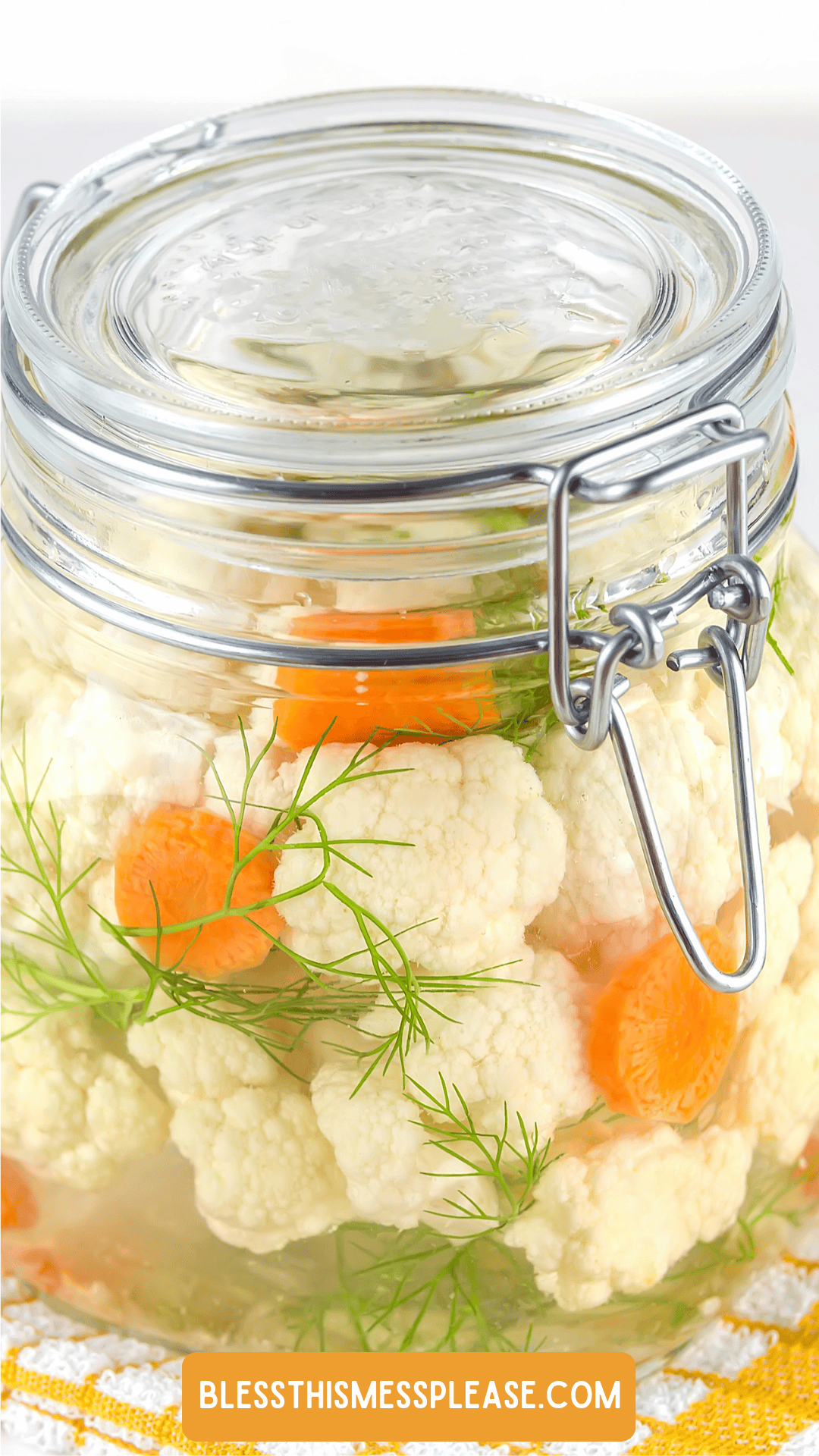 A glass jar filled with pickled cauliflower, sliced carrots, and fresh dill sprigs in brine, sealed with a metal clasp lid. Learn how to preserve cauliflower at blessthismessplease.com, displayed at the bottom.