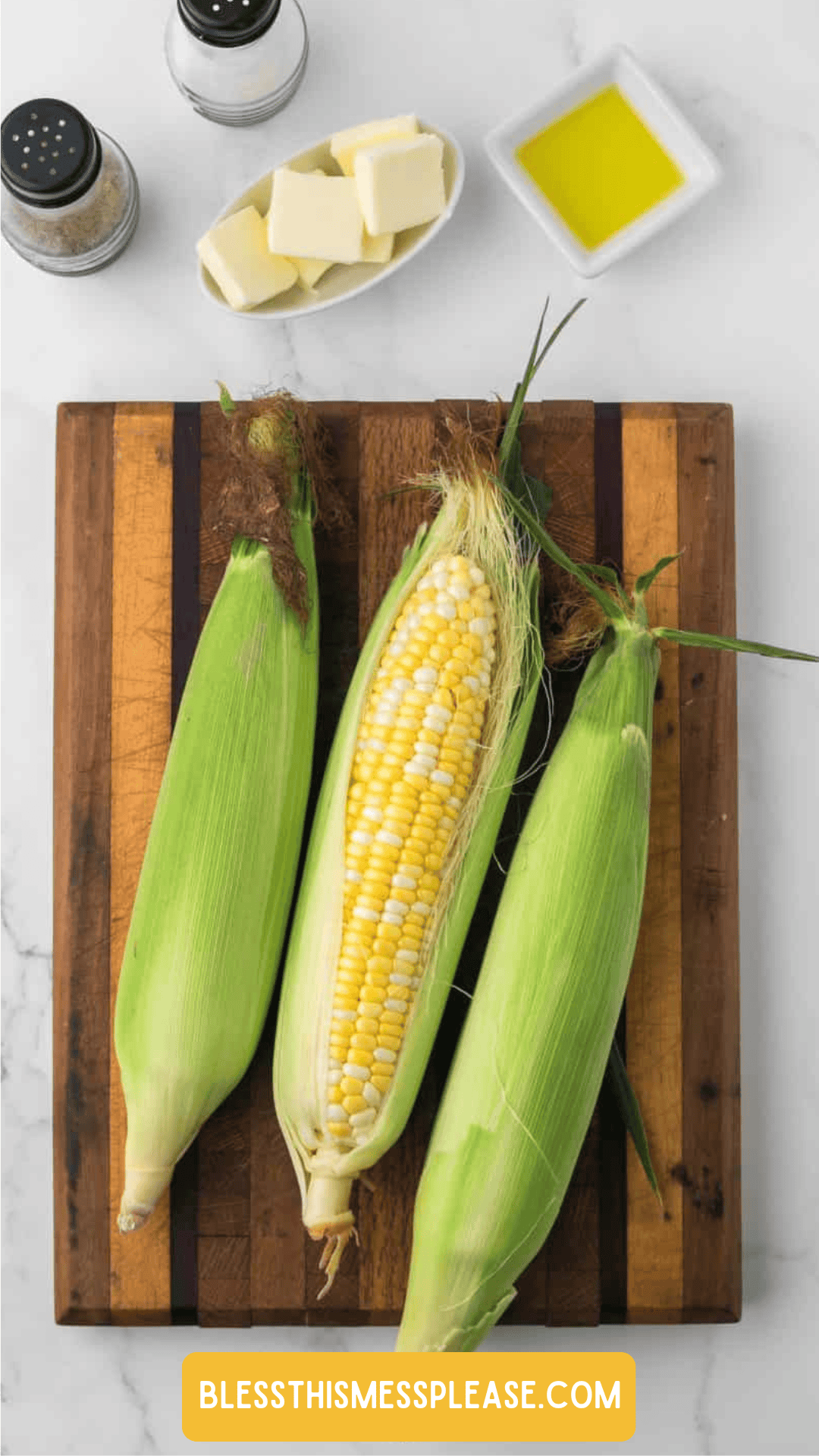 Three ears of corn, one partially husked, rest on a wooden cutting board. Nearby are salt and pepper shakers, a dish of butter, and a small bowl of oil—perfect for learning how to preserve corn at home.