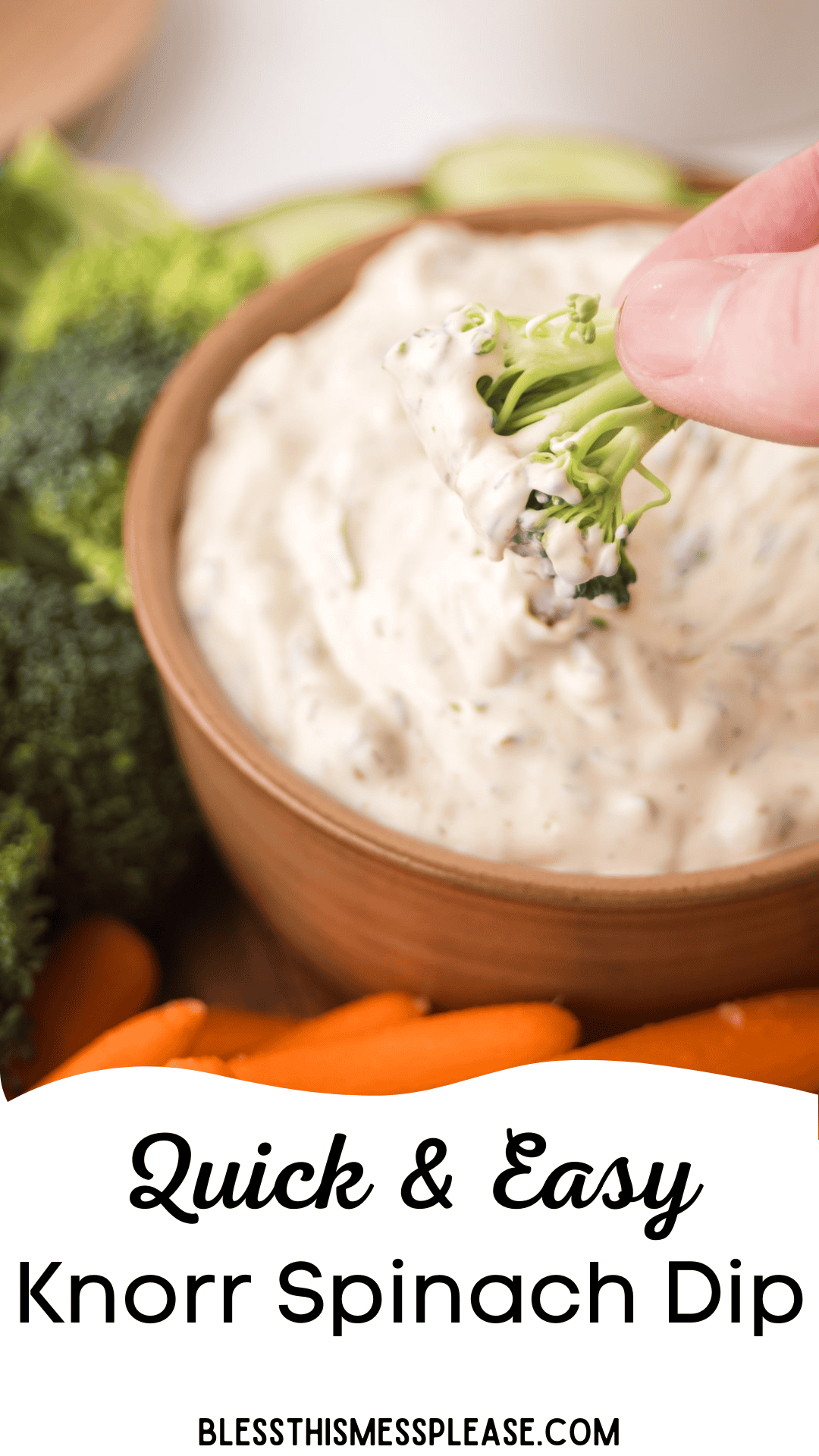 A hand dips a piece of broccoli into creamy knorr veggie spinach dip in a wooden bowl. Fresh vegetables, including broccoli and carrots, surround the bowl. Text reads Quick & Easy Knorr Spinach Dip and blessthismessplease.com.