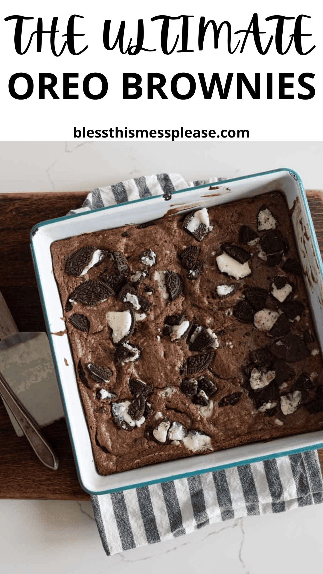 A pan of freshly baked Oreo brownies sits on a striped kitchen towel, with chunks of Oreo cookies scattered on top. A metal spatula rests beside the pan on a wooden board, ready to serve these irresistible oreo brownies.