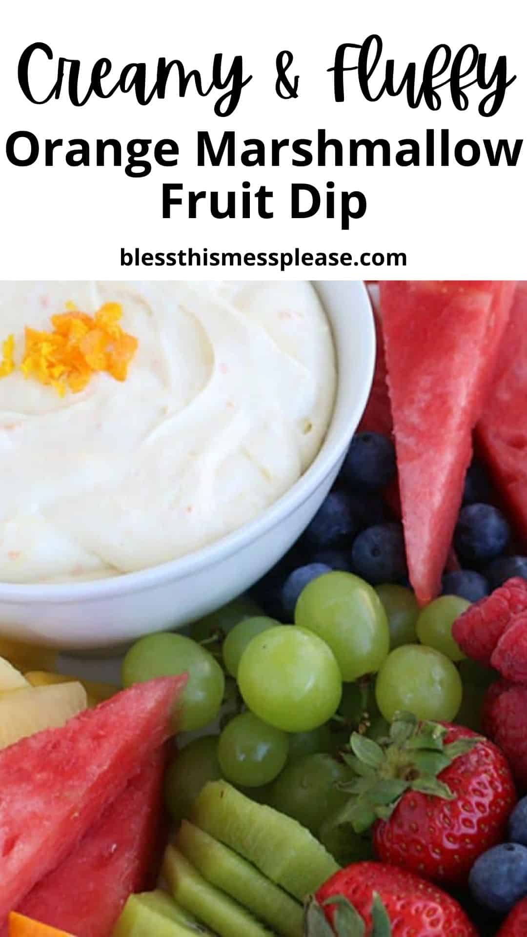 A bowl of creamy orange marshmallow fruit dip recipe, garnished with orange zest and surrounded by fresh fruit like watermelon, grapes, blueberries, and kiwi slices. Text above reads “Creamy & Fluffy Orange Marshmallow Fruit Dip.”.