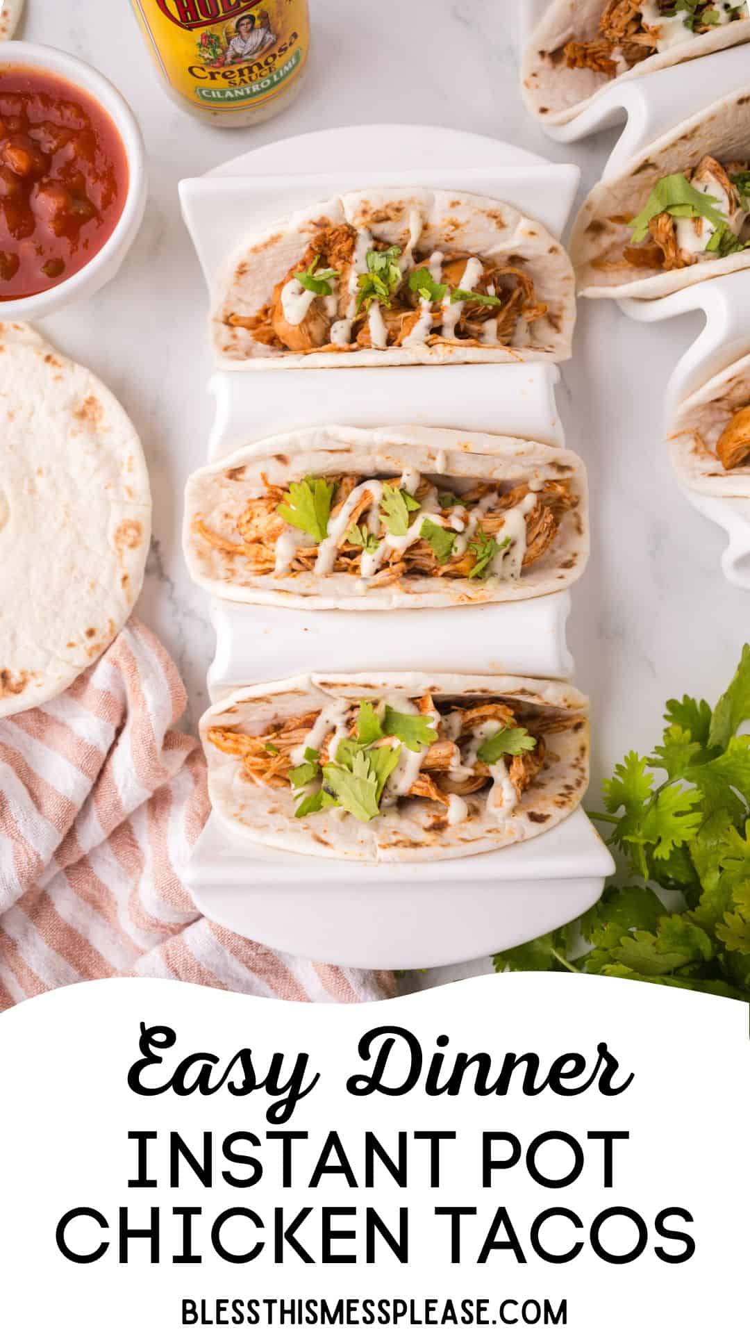 Three instant pot chicken tacos topped with sauce, cheese, and cilantro sit in a white taco holder. Nearby are a flour tortilla, a bowl of salsa, hot sauce, fresh cilantro, and a striped napkin. Text reads: Easy Dinner Instant Pot Chicken Tacos.