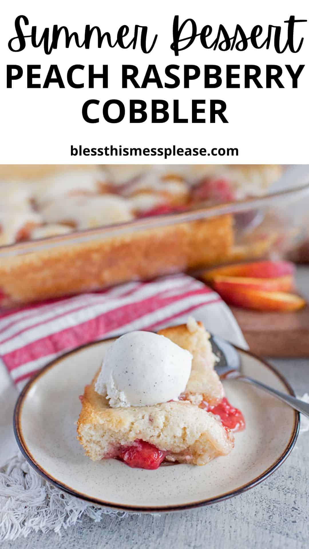 A slice of peach raspberry cobbler topped with a scoop of vanilla ice cream sits on a plate with a spoon. In the background, a baking dish of peach raspberry cobbler and fresh peach slices complete the scene.