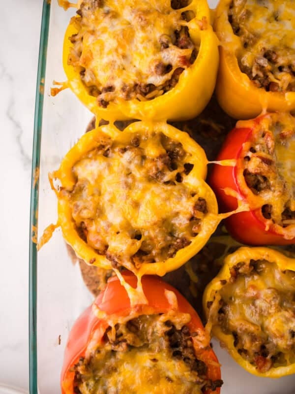 A glass baking dish filled with stuffed peppers with ground beef and melted cheese, featuring vibrant yellow and red bell peppers, viewed from above on a white surface.