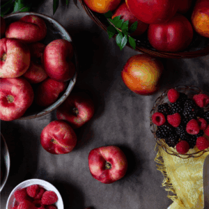 A flat lay of various fresh fruits, including nectarines, peaches, raspberries, and blackberries on a dark surface, with a yellow cloth and a BLESSTHISMESSPLEASE.COM label at the bottom—perfect inspiration for learning how to preserve plums.