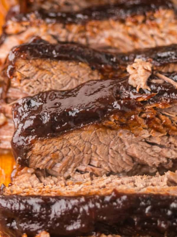 Close-up of several thick slices of slow cooker brisket with a dark, glossy layer of barbecue sauce on top, displayed on a wooden cutting board.