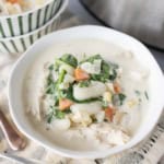 A bowl of creamy soup filled with gnocchi, shredded chicken, spinach, carrots, and onions, with another bowl of soup in the background on a striped cloth.