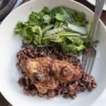 A white plate with cranberry chicken topped with sauce and cherries on a bed of rice, served alongside a green leafy salad with cucumber slices. A fork rests on the plate.