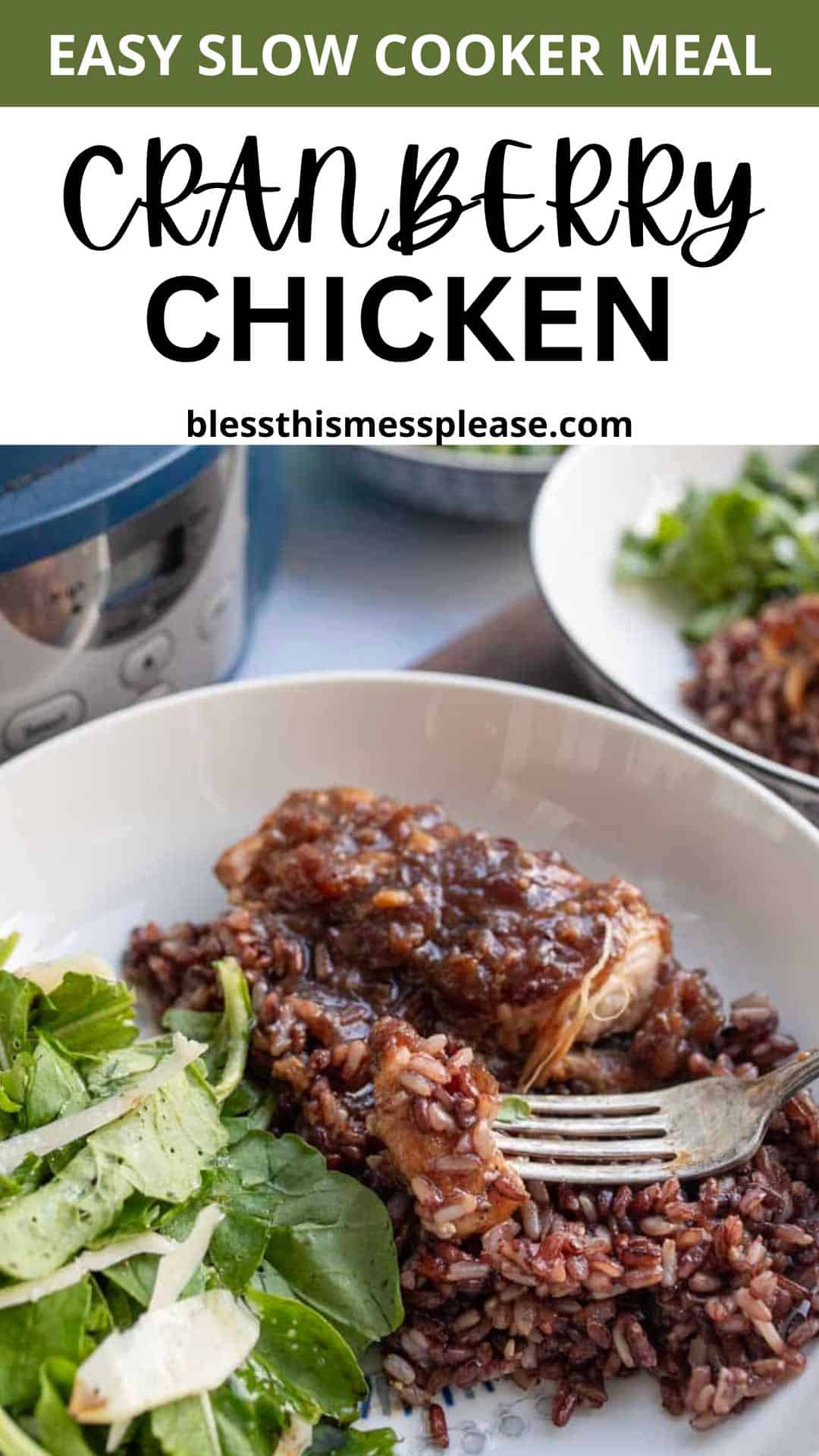 A white bowl with cranberry chicken on purple rice, garnished with sauce, sits next to a fresh green salad. A fork rests on the bowl. Another plate and a slow cooker are in the background. Text above highlights “Easy Slow Cooker Meal: Cranberry Chicken.”.