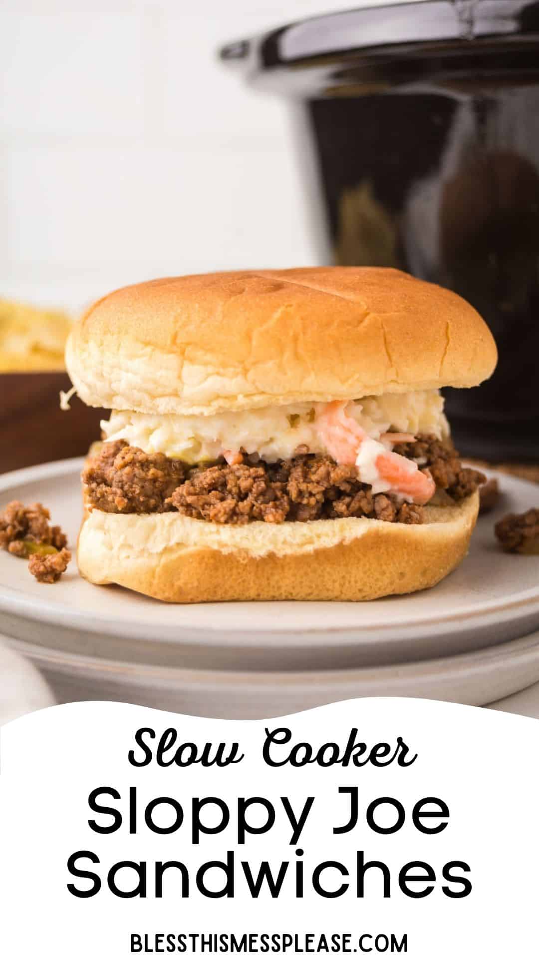 A plate holds a Sloppy Joe sandwich with ground meat filling and coleslaw on a bun. A crock pot is in the background. Text reads: Crock Pot Sloppy Joes Sandwiches. blessthismessplease.com.