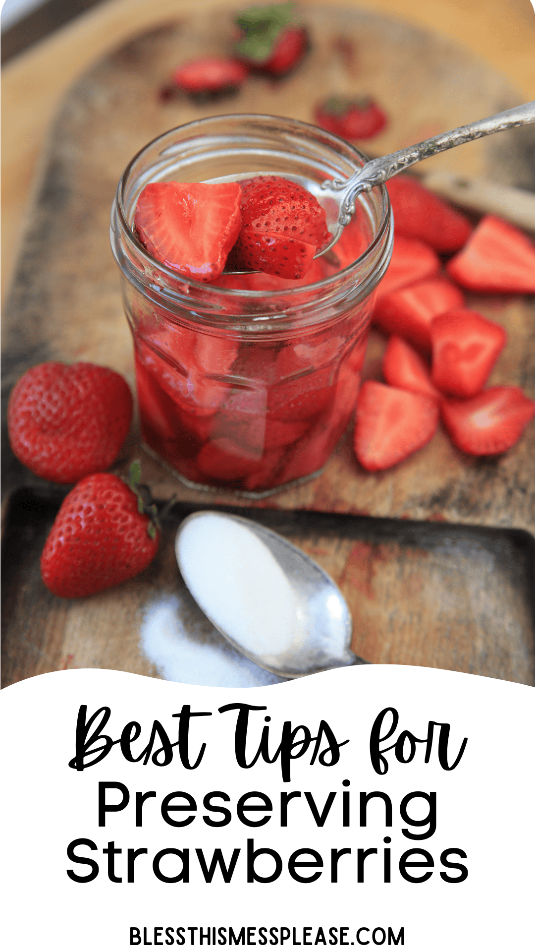 A glass jar filled with sliced strawberries and a spoon sits on a wooden cutting board, surrounded by whole and sliced strawberries. Wondering how to preserve strawberries? Best Tips for Preserving Strawberries is written at the bottom.