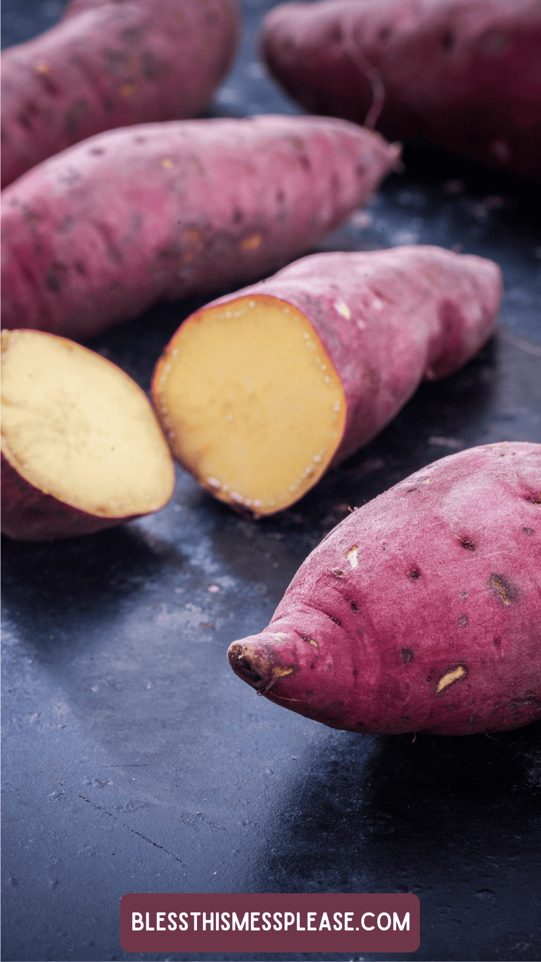 Whole and halved raw sweet potatoes with reddish-purple skins and pale yellow flesh rest on a dark surface. Curious about how to preserve sweet potatoes? Find tips at the label: blessthismessplease.com.