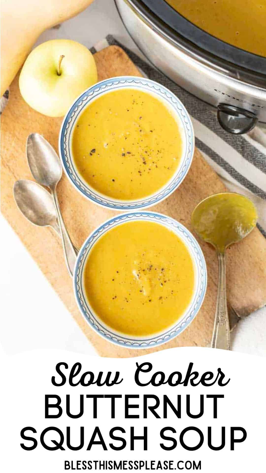 Two bowls of creamy slow cooker butternut squash soup sit on a wooden board with spoons, next to a fresh apple and a slow cooker. The text below reads: “Slow Cooker Butternut Squash Soup blessthismessplease.com.”.