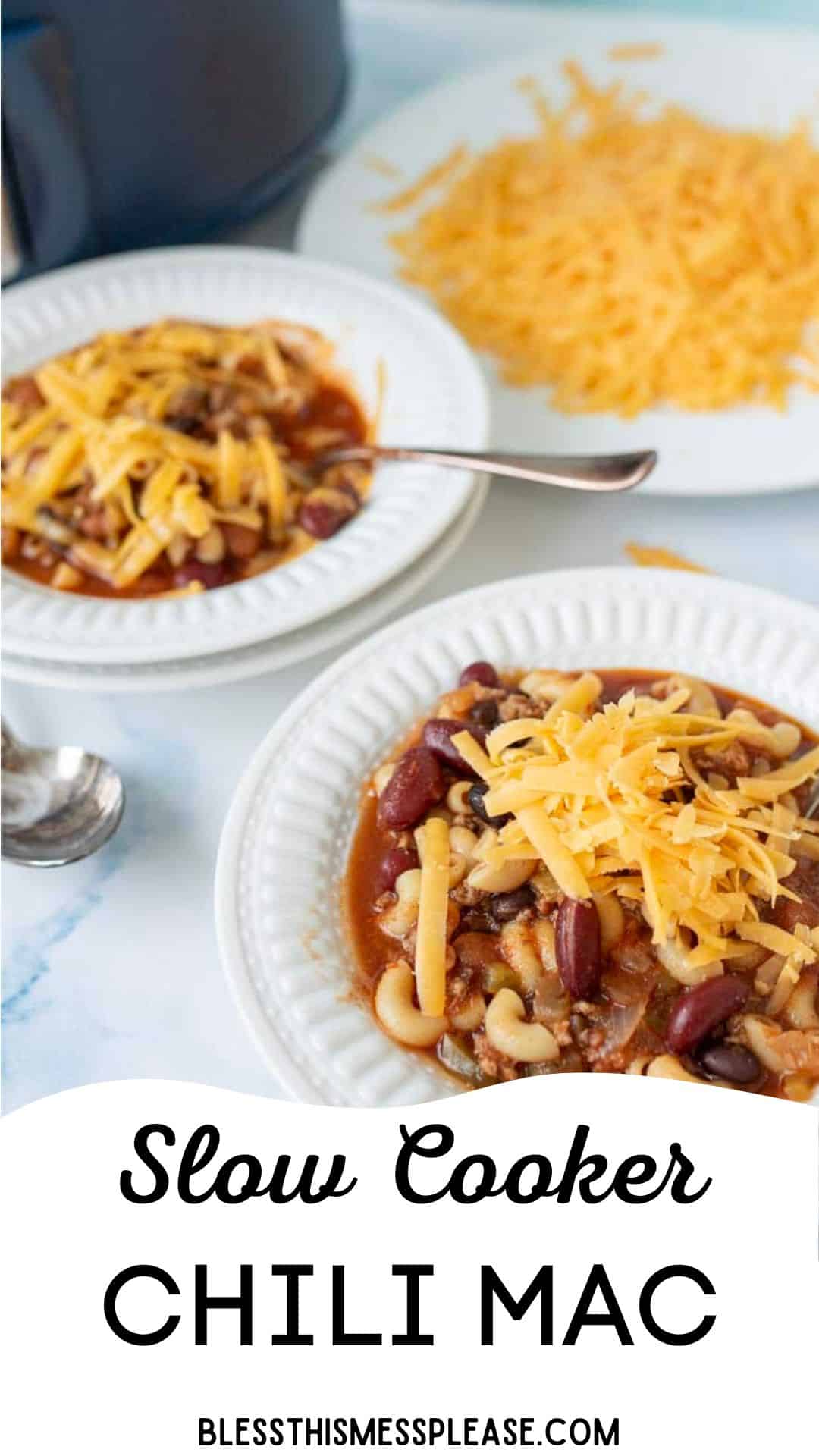 Two white plates filled with slow cooker chili mac, topped with shredded cheddar cheese, with extra cheese on a plate in the background. A spoon rests beside one plate. Text reads: Slow Cooker CHILI MAC bless this mess please dot com.