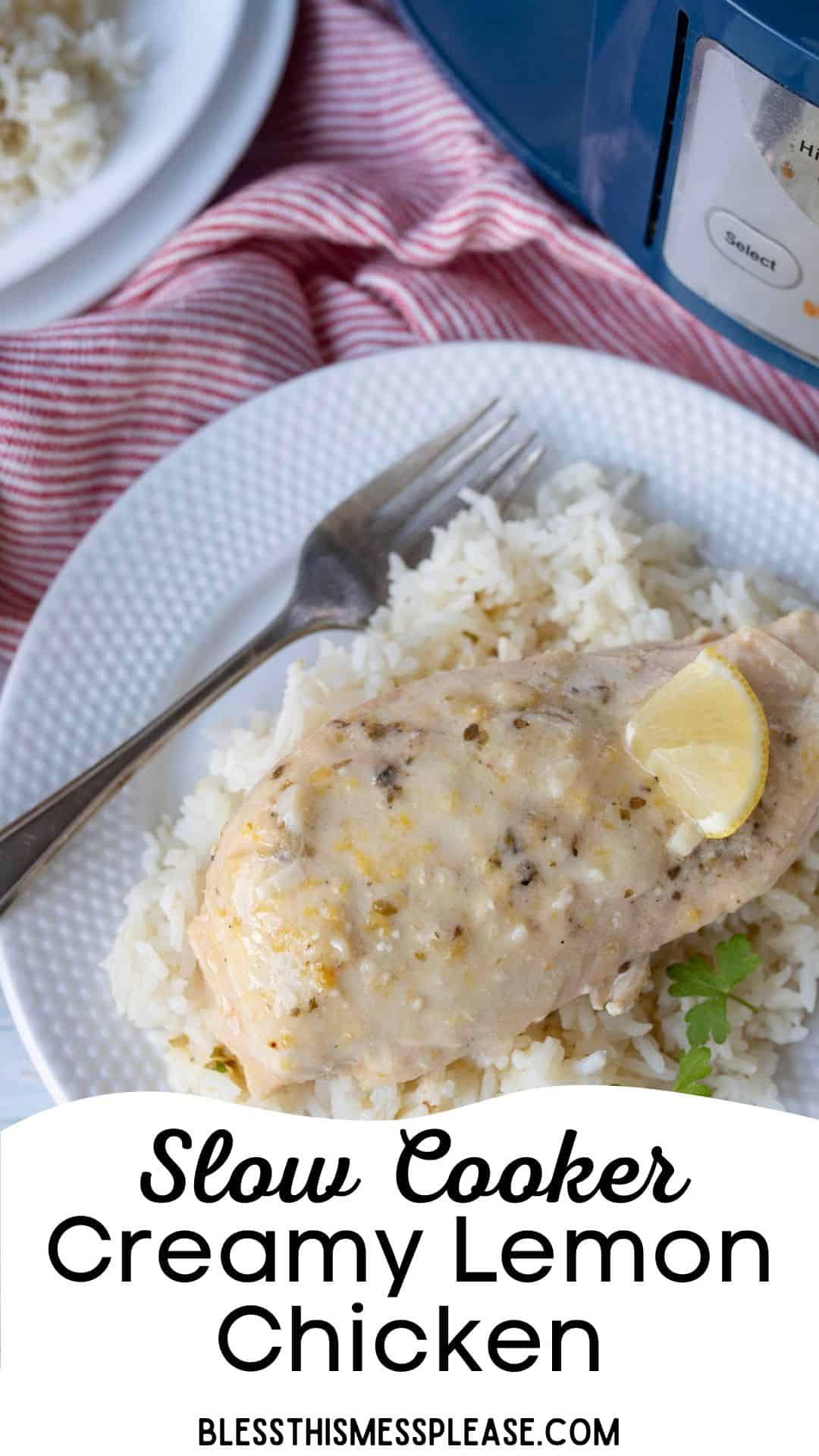 A plate of rice topped with creamy slow cooker lemon chicken breast, garnished with a lemon wedge. A fork rests on the plate next to the chicken. Part of a slow cooker and another plate are visible in the background.
