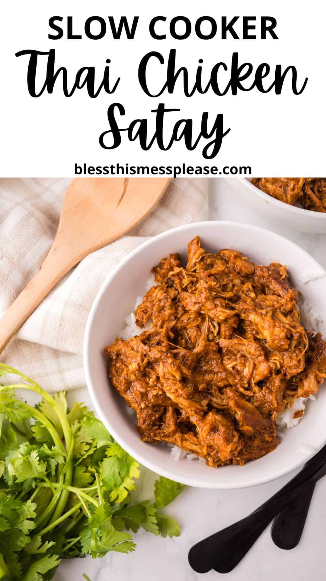 A white bowl filled with slow-cooked Thai chicken satay recipe served over rice sits on a marble counter with black utensils, fresh cilantro, a wooden spoon, and a beige cloth nearby.