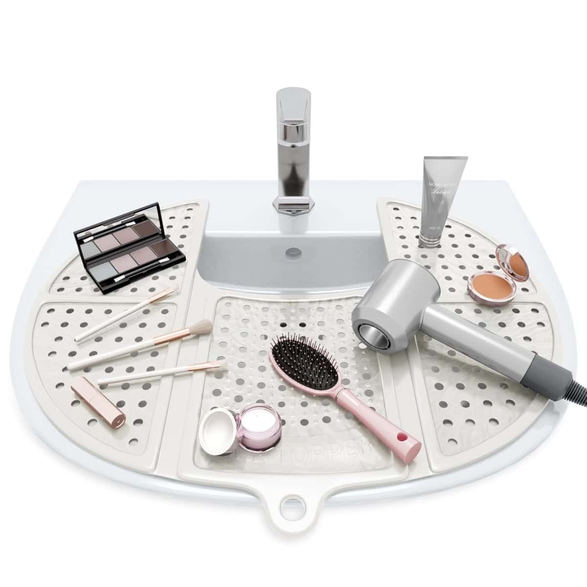 A bathroom sink with a gray silicone mat covering the counter, holding makeup brushes, a hair dryer, makeup products, a hairbrush, and an eyeshadow palette.
