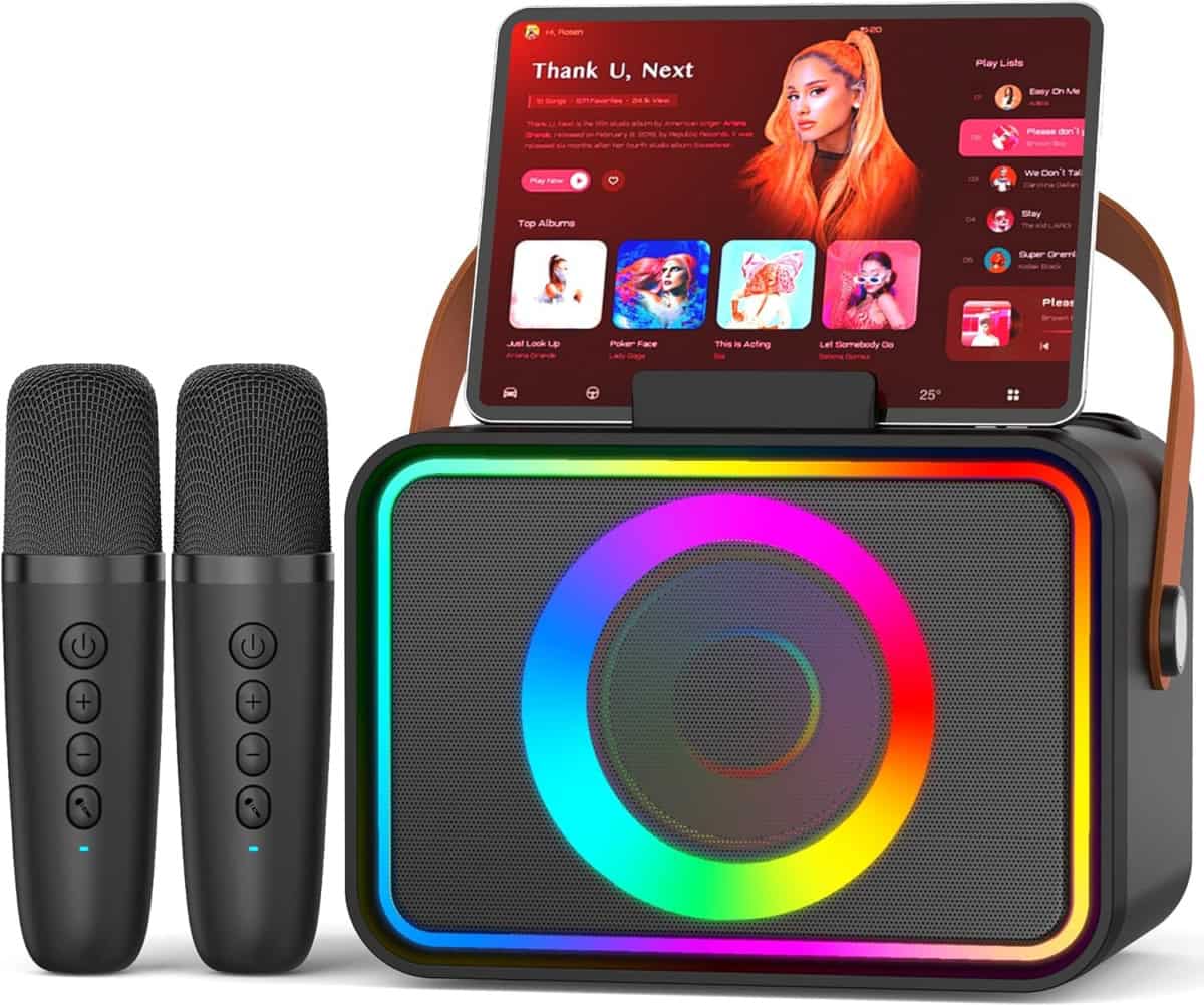 A portable karaoke machine with colorful LED lights, a tablet displaying a music playlist on top, and two wireless microphones placed beside it.
