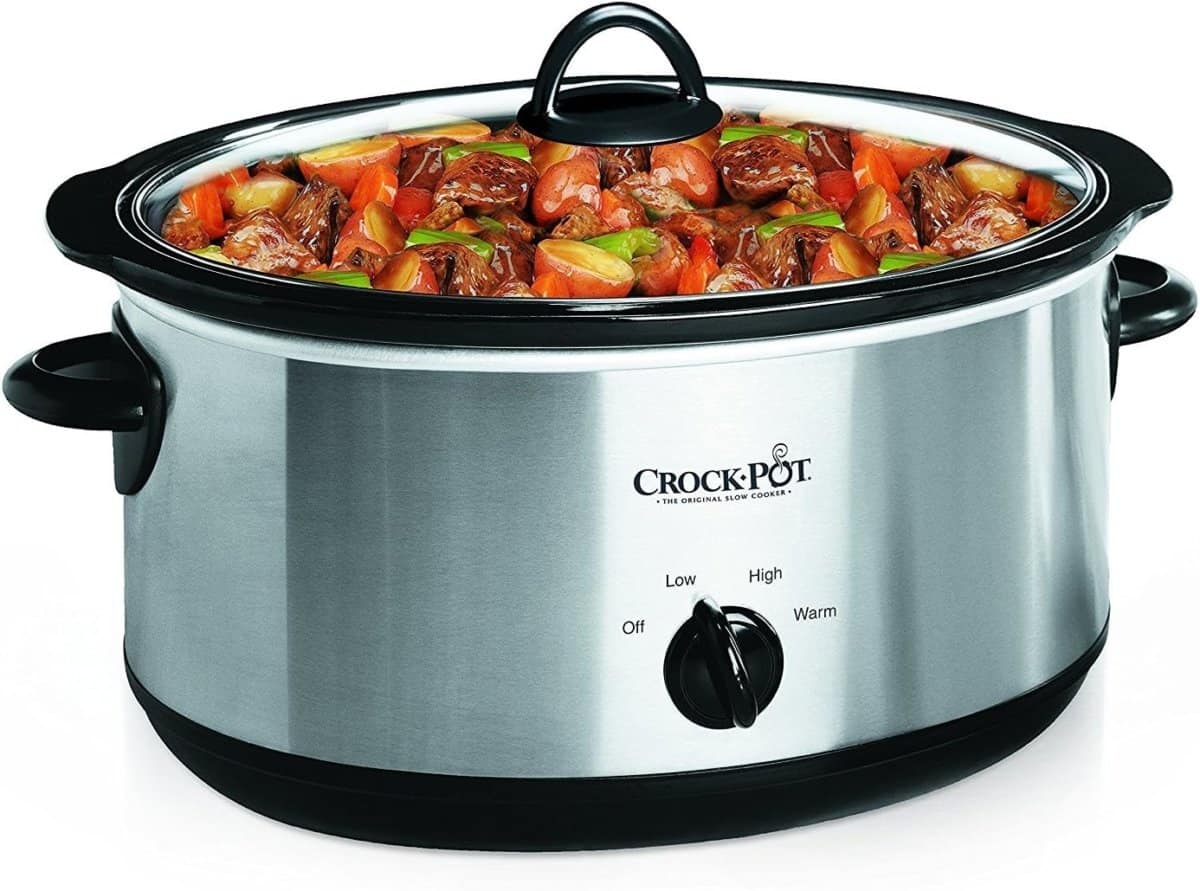 A stainless steel Crock-Pot slow cooker filled with a stew of meat and chopped vegetables, with the lid partially on and the control knob set to low.