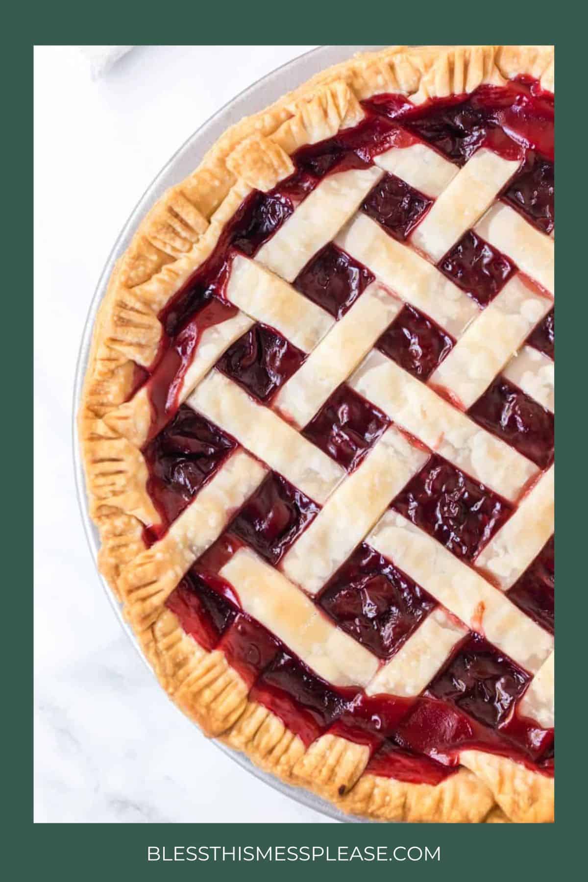 A close-up of a cherry pie with a golden, lattice crust and crimped edges—perfect for christmas pies. The pie is partially shown on a white surface, with the website blessthismessplease.com at the bottom.