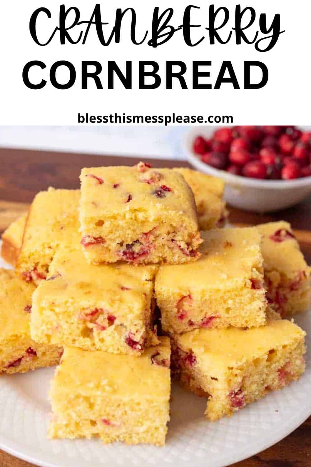 A plate of square cranberry cornbread slices is stacked on a table, with a bowl of fresh cranberries in the background. The text above reads Cranberry Cornbread and blessthismessplease.com.