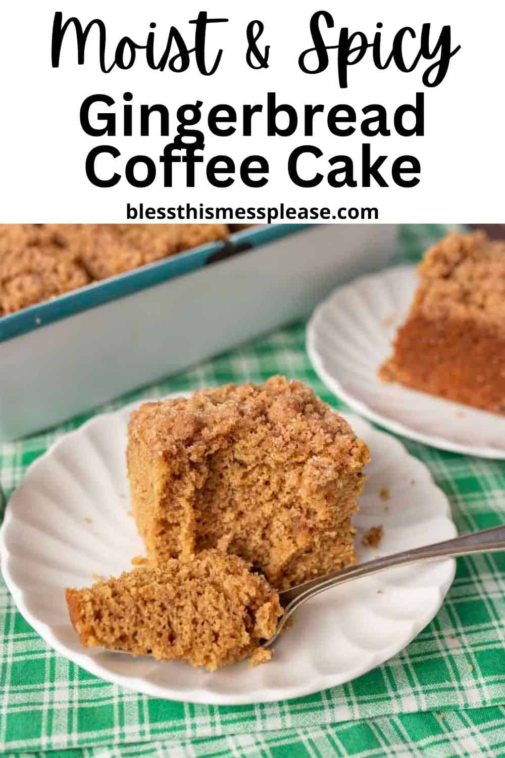A slice of gingerbread coffee cake with crumb topping sits on a white plate with a fork and a piece cut off. Another slice of gingerbread coffee cake and a blue baking dish rest in the background, all atop a green plaid tablecloth.