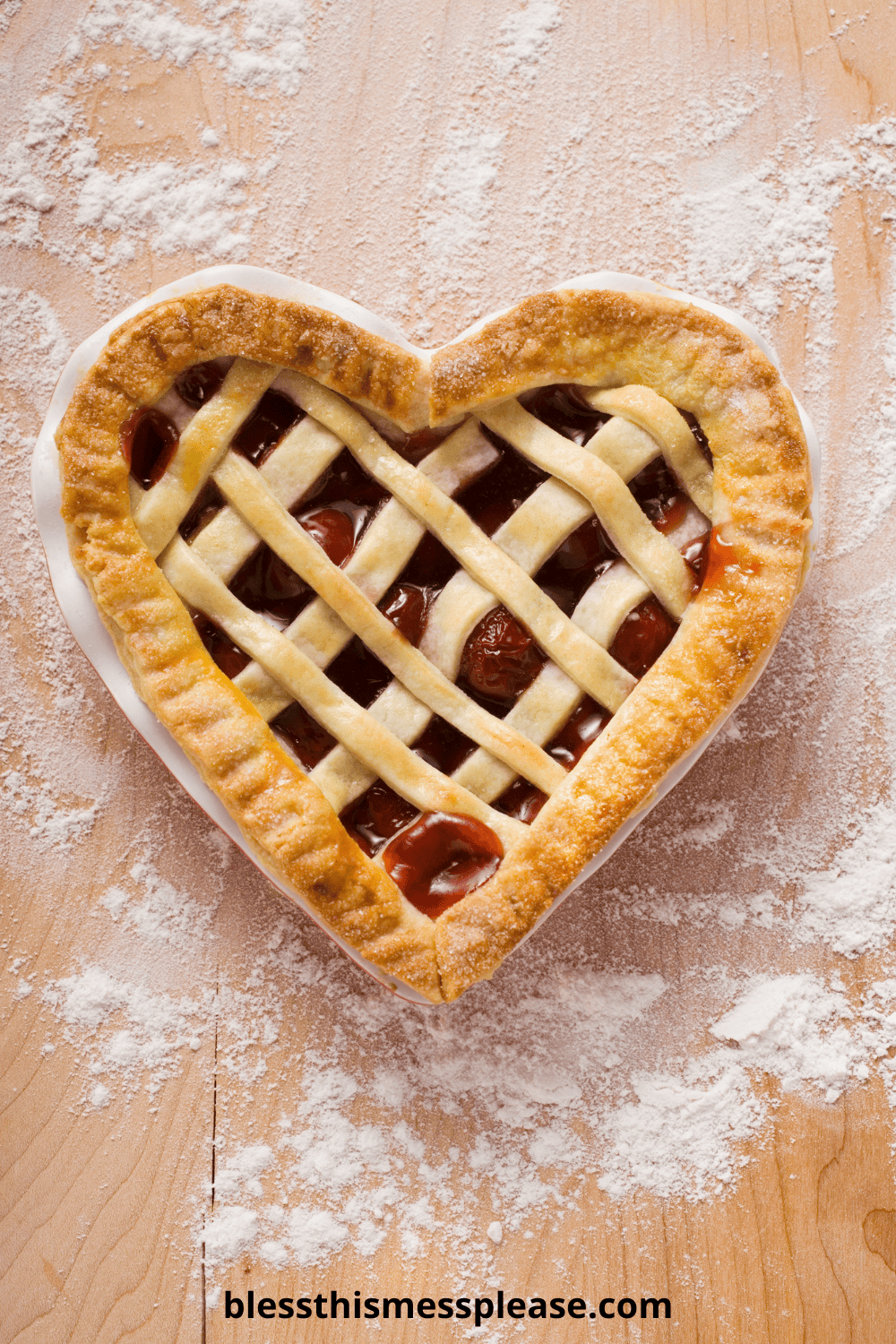 A heart-shaped cherry pie with a lattice crust sits on a floured wooden surface. The golden brown edges and peek of cherry filling hint at homemade goodness—learn how to make pie crust at blessthismessplease.com.