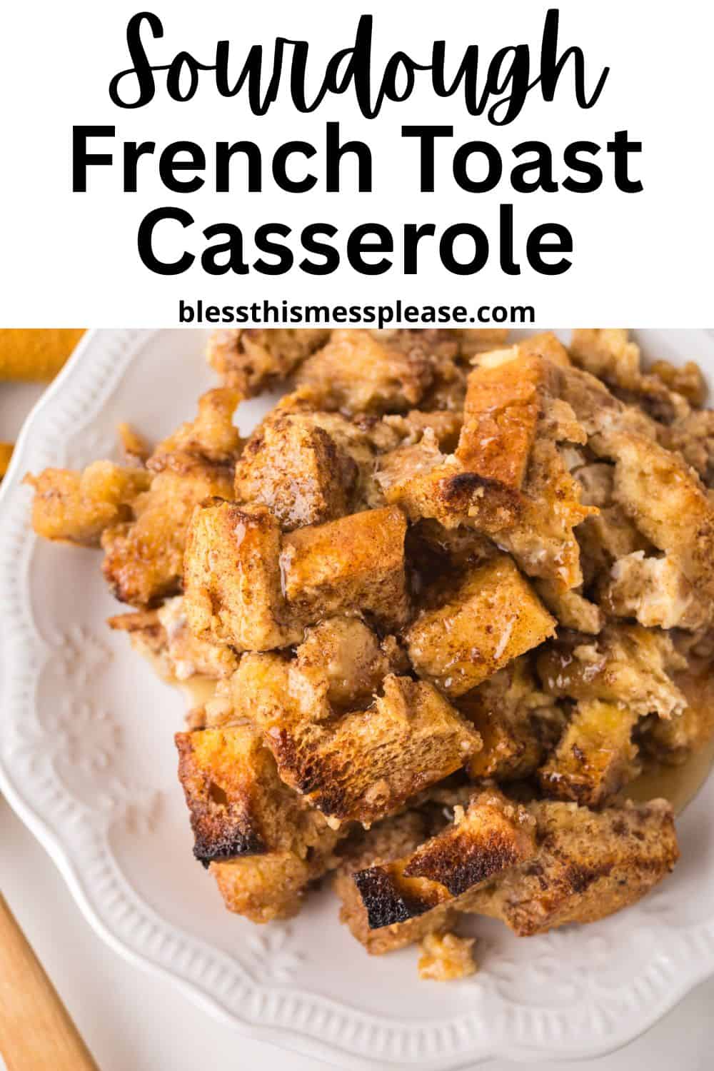 Plate with a serving of golden-brown sourdough french toast casserole, made with chunky bread pieces, sitting on a white decorative plate. Text above reads: “Sourdough French Toast Casserole - blessthismessplease.com.”.