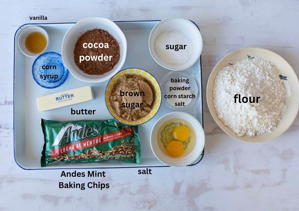 Baking ingredients arranged on a tray, including bowls of flour, cocoa powder, sugar, brown sugar, corn syrup, vanilla, baking powder, cornstarch, salt, two eggs, butter, and a package of Andes Mint Baking Chips.