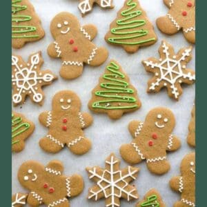 Christmas cookies shaped like gingerbread people, Christmas trees with green icing, and snowflakes with white icing, arranged on parchment paper. Website text BLESSTHISMESSPLEASE.COM at the bottom.