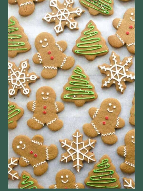Christmas cookies shaped like gingerbread people, Christmas trees with green icing, and snowflakes with white icing, arranged on parchment paper. Website text BLESSTHISMESSPLEASE.COM at the bottom.