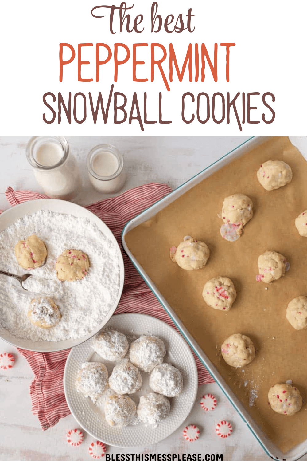 Overhead view of peppermint snowball cookies—some coated in powdered sugar on a plate, others uncoated on a baking tray lined with parchment. Two bottles of milk, peppermint candies, and a red-striped cloth surround the festive treats.