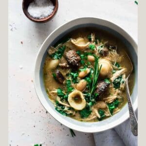 sausage, pasta, greens soup in white bowl on light gray background featuring winter soups.