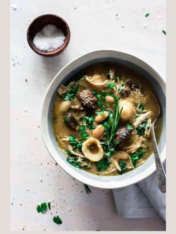sausage, pasta, greens soup in white bowl on light gray background featuring winter soups.