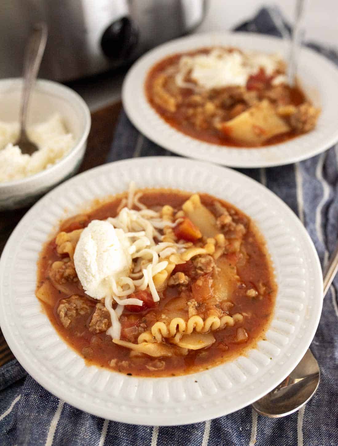 Two plates of lasagna soup in slow cooker style, filled with noodles and topped with cheese.