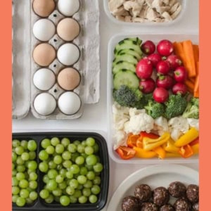 A variety of healthy foods are arranged on a table, including eggs, cooked chicken strips, sliced vegetables, grapes, and round chocolate snack balls. The image has an orange border and the website blessthismessplease.com at the bottom.