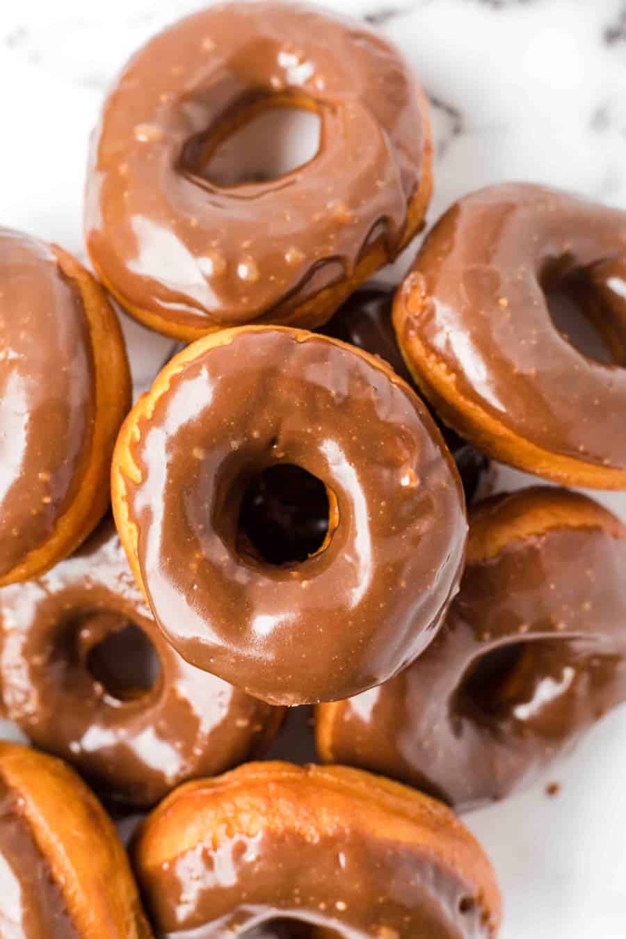 A close-up of several golden-brown donuts topped with shiny chocolate glaze, arranged closely together on a white surface.
