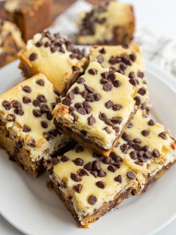 A plate of chocolate chip cheesecake bars stacked on top of each other, featuring a creamy top layer with mini chocolate chips and a dense, brownie-like base.