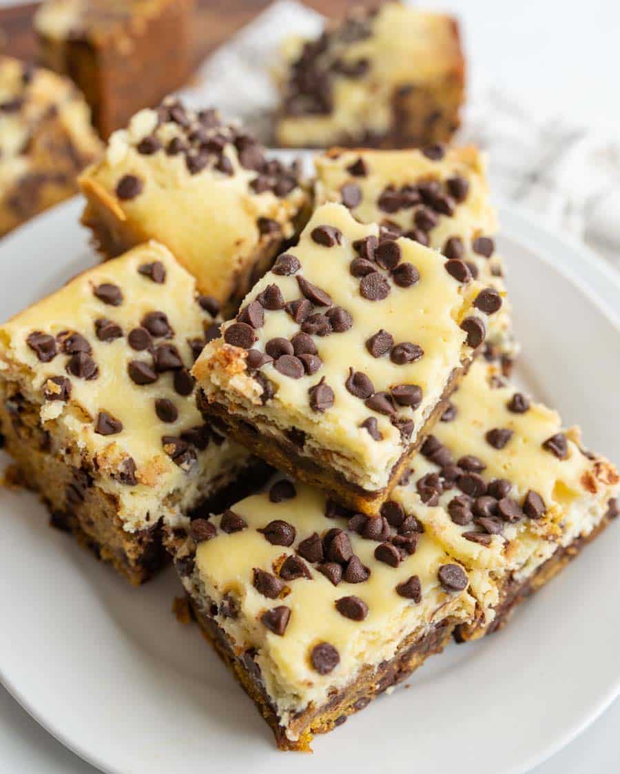 A plate of chocolate chip cheesecake bars stacked on top of each other, featuring a creamy top layer with mini chocolate chips and a dense, brownie-like base.